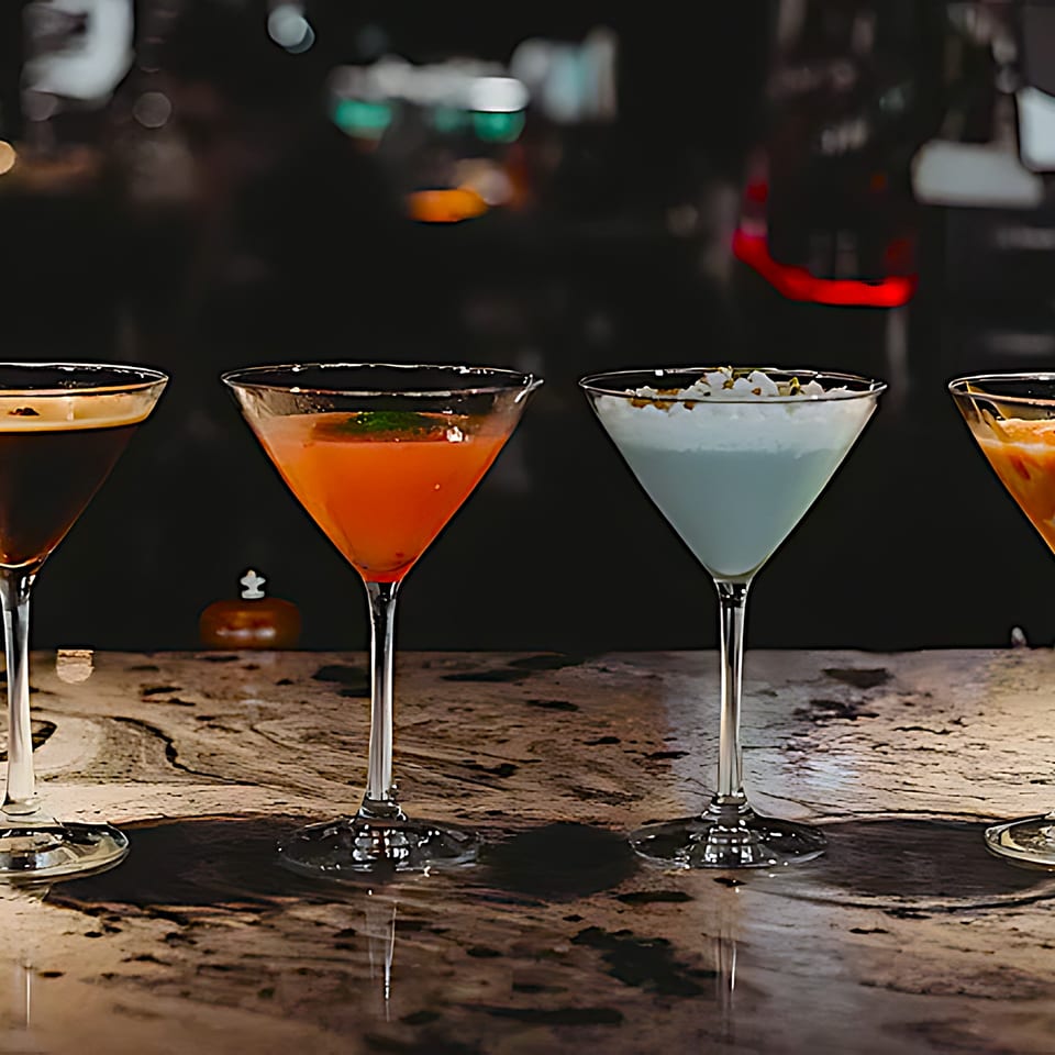 Four colorful cocktails in martini glasses on a dark bar at Mickey's Downtown Bistro.
