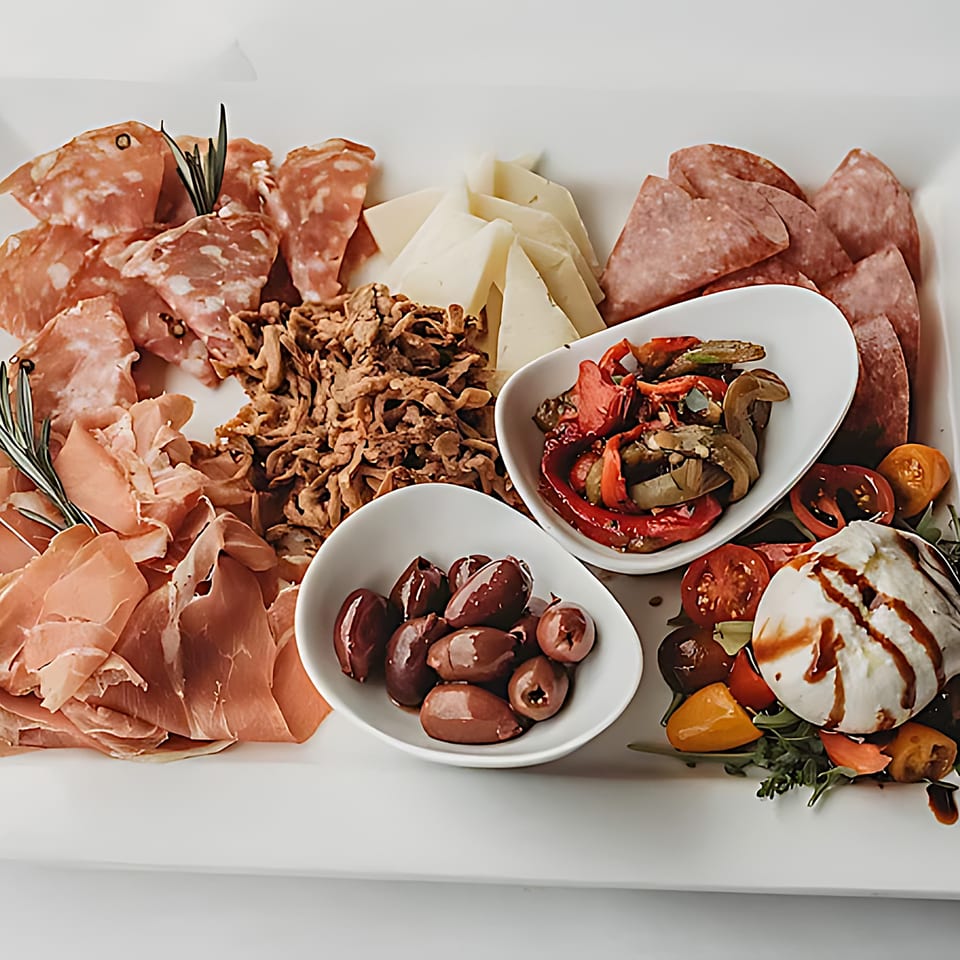A charcuterie board with various meats, cheeses, olives, roasted vegetables, and burrata cheese.