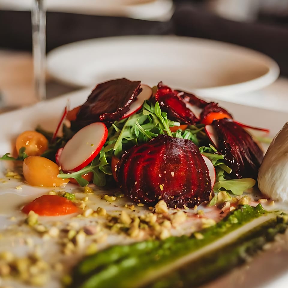 A vibrant bistro salad with roasted beets, arugula, radishes, tomatoes, and pistachios on a white plate.