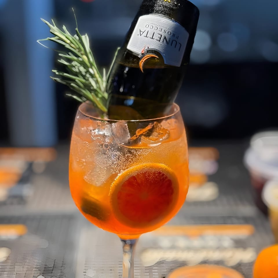 A vibrant orange cocktail with a mini Lunetta Prosecco bottle, rosemary, and orange slice at Mickey's Downtown Bistro.