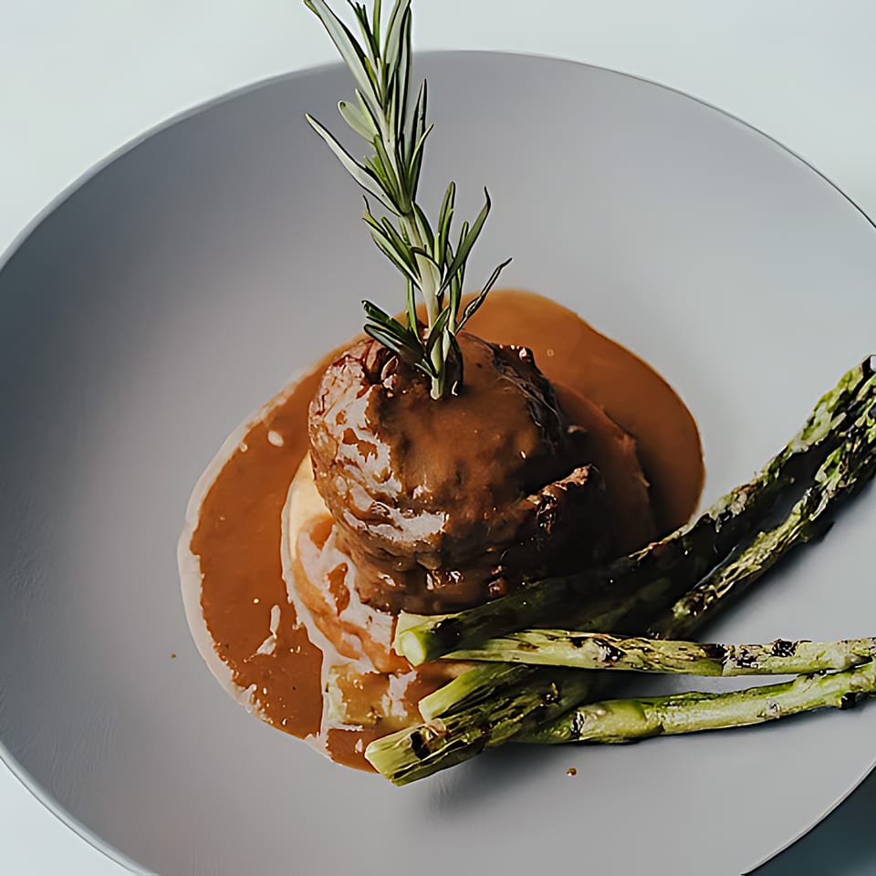 Mickey's Downtown Bistro's meatball with gravy, mashed potatoes, and roasted asparagus on a gray plate.
